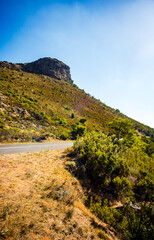 Hillside, grasses, outcrop, winding road, sunny, clear blue sky.