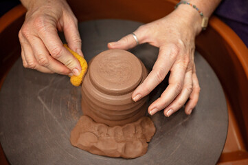 Artisan smoothing a clay piece with a sponge on a pottery wheel