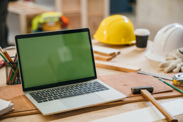 Laptop with a green screen on a wooden workbench alongside a hammer in a carpenter's shop. Ideal for showcasing a carpenter's workspace, DIY projects, and mockup displays