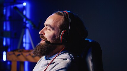Smiling man plays online multiplayer spaceship videogame with friends, chatting using headphones...