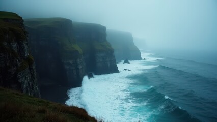 Foggy coastal cliffs with waves crashing against the rocky shore.