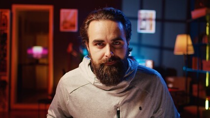 Fototapeta premium Portrait of happy man focused on completing videogame in neon lit living room. Smiling gamer having gaming session, concentrating while competing in multiplayer tournaments