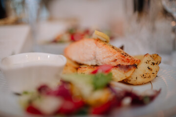 Close-up of a gourmet meal featuring grilled salmon with lemon, roasted potatoes, fresh salad, and a side of creamy sauce, served on an elegant plate.