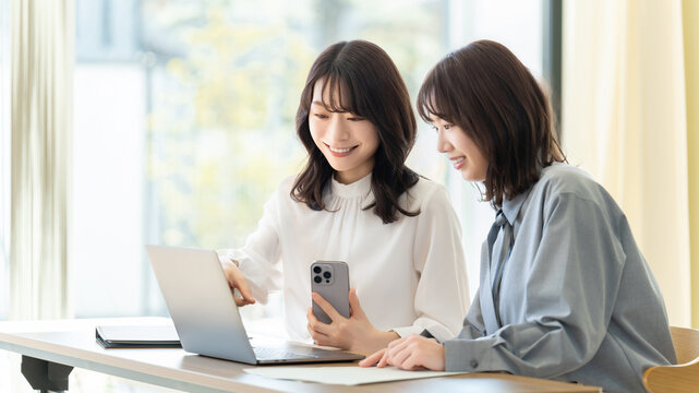 パソコンとスマホを使って話す2人の女性・ビジネスウーマン