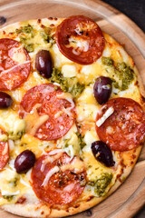 Pizza with chorizo ​​sausage, mozzarella and cheddar cheese, olive pesto and kalamata olives. Wooden background. Soft focus. Close up.	