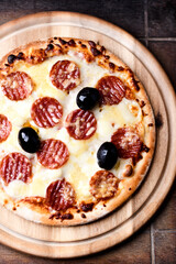 Pizza with salami, mozzarella and cheddar cheese. Wooden background. Soft focus. Top view.  Close up.