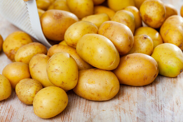Freshly washed potatoes, poured out of a bucket on a wooden table. Ingredients for cooking..