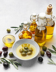 Bottles and bowls of golden olive oil with olives and olive branches residing on table