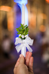 A close-up shot of a hand holding a white candle adorned with greenery and a lace ribbon. The...