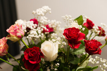 Close-up of a beautiful flower arrangement featuring red and white roses and small white flowers. The colors and textures create a romantic and elegant feel.
