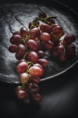 A close-up shot of a bunch of ripe red grapes resting on a textured black plate