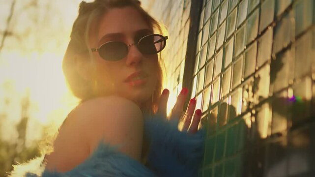 model in glasses and blue fur coat poses for camera. at sunset blonde girl poses. fashion trend