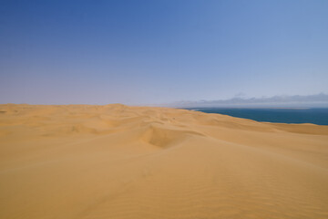 Endless golden dunes stretch towards the horizon, where the vast Namib Desert meets the Atlantic Ocean in the breathtaking wilderness of Sandwich Harbour, Namibia.