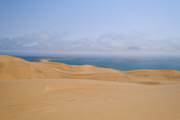Sweeping sand dunes descend into the deep blue waters of the Atlantic, showcasing the stunning contrast of Namibia’s remote Sandwich Harbour, where the desert meets the sea.