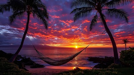 Fototapeta premium Sunset Paradise A hammock strung between two swaying palm trees overlooking a brilliant vibrant sunset on a tropical beach with the shimmering ocean in the background