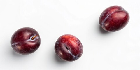 Obraz premium Three plums arranged on a light background, highlighting their rich color and smooth texture.