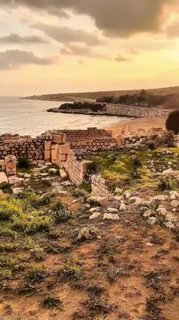 Eleusa Sebaste ancient ruins by the Mediterranean Sea at sunset. Weathered stone walls and remnants of structures from the Roman era, surrounded by coastal vegetation and overlooking the sandy shore.