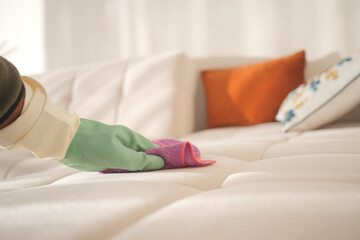 Cleaning a white sofa with a colorful cloth and gloves