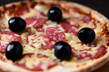 Pizza with salami, mozzarella and cheddar cheese. Wooden background. Soft focus. Close up.