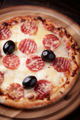 Pizza with salami, mozzarella and cheddar cheese. Wooden background. Soft focus. Close up.