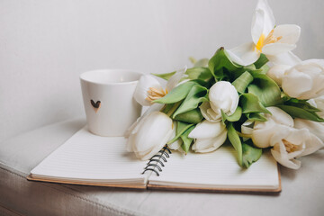 Beautiful white cup with hot coffee, notepad and a bouquet of white tulips. Composition with copy space. 