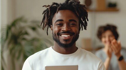 Happy young man with dreadlocks holding a tablet indoors smiling