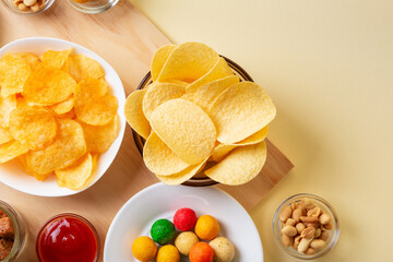 Different snacks such as chips,  salted nuts, wasabi nuts on wooden desk on beige background.