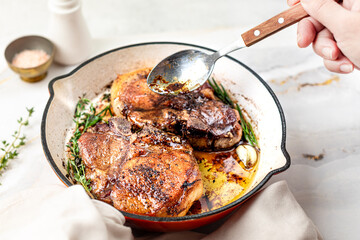 Pan-fried and baked steaks on a bone with garlic, butter and thyme on a marble table.