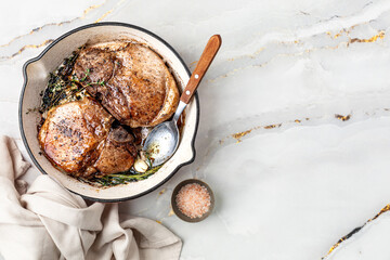 Pan-fried and baked steaks on a bone with garlic, butter and thyme on a marble table.