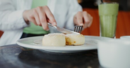 A woman eats cheesecakes, cutting them with a knife, close-up of female hands, no face