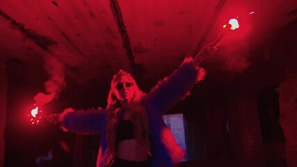dark room. girl in blue fur coat lights flare. flare burns red. girl with flare. trend and fashion