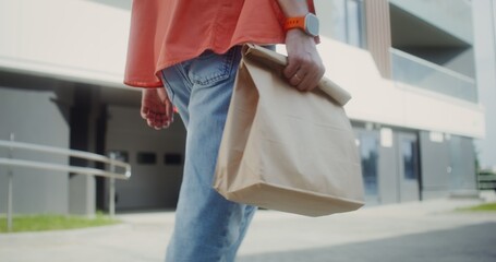 A man carries a paper bag with ready-made food walking around the city, close-up of his hands, no face