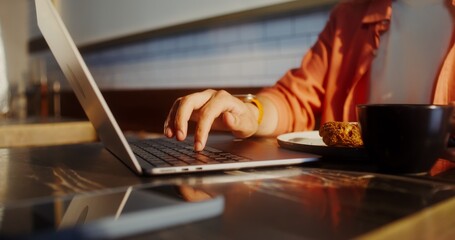 A man uses a laptop while sitting at a table in a cafe, close-up of a man's hands, no face