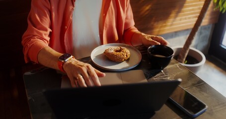 A stylish young man with glasses uses a laptop and drinks coffee sitting at a table in a cafe