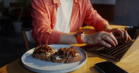 A stylishly dressed man uses a laptop while sitting at a table in a cafe