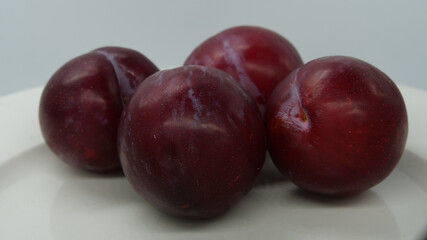 Close-up of four deep red plums on a white plate