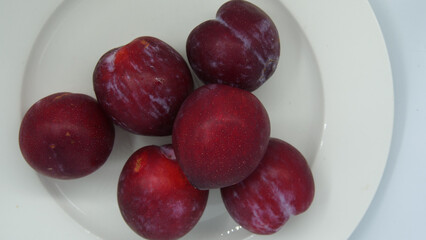 Top down view of deep red plums on a white plate