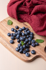 Fresh blueberries on a wooden board with mint leaves and red fabric. Balanced and warm composition. Concept of healthy cooking, natural food and freshness