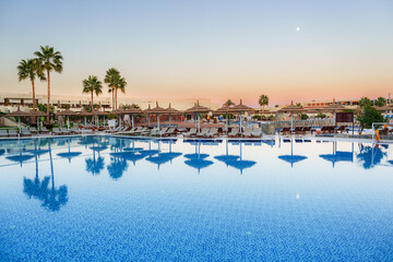 Relaxing evening at a tranquil poolside resort featuring palm trees and reflecting waters