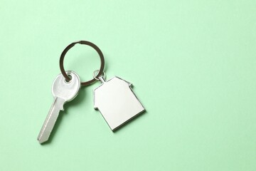 Metallic key with keychain and wooden house on color background