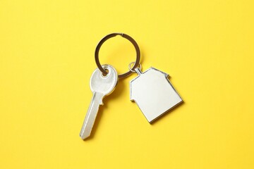 Metallic key with keychain in shape of house on color background