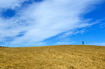Small silhouette of a tourist standing on a grassy hill. Early spring trip.
