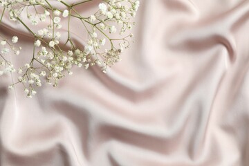 Beige silk satin. Shiny smooth fabric with gypsophila. Soft folds. Luxury background with space for...