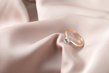 Beautiful shiny gold engagement ring with large diamond gemstone on silk fabric background
