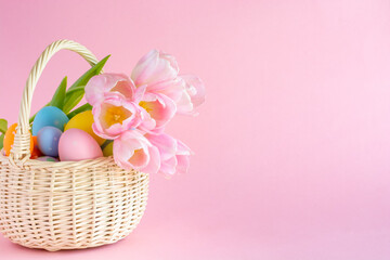 Basket with Easter eggs and tulips on a pink paper background, copy space. High quality photo