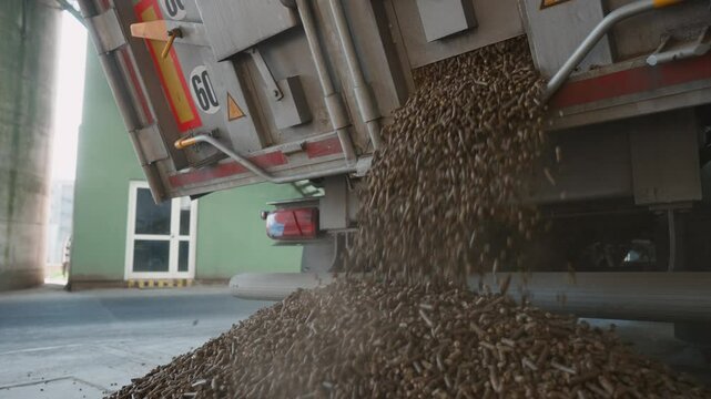 View in slow motion of brown cylindrical pellets being unloaded in a large-scale industrial food production facility