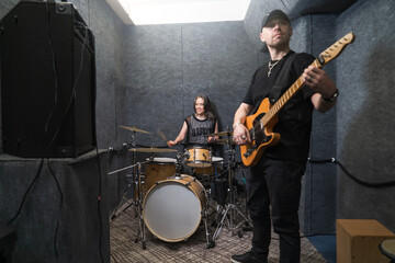 Fototapeta premium guitarist and female drummer playing together in professional soundproof rehearsal studio. Rock band members practicing live performance and sound arrangement.