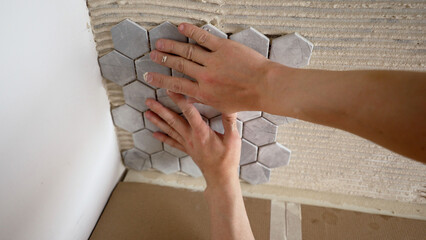 Tiler installing hexagonal mosaic tiles on bathroom wall