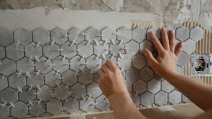 Tiler installing hexagonal marble tiles on a wall using tile spacers, creating a stylish and modern...