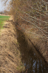 drainage ditch with dark water next to a harvested field in late winter